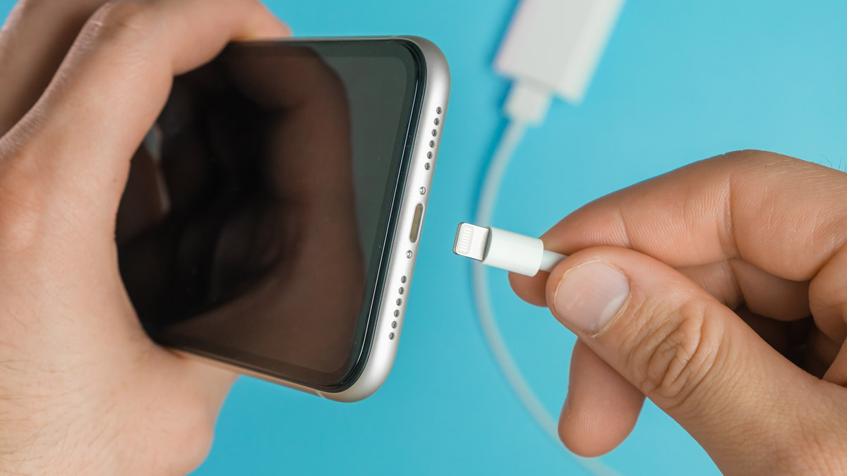 Close-up of a hand plugging a charging cable into a smartphone.